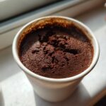 Close-up of rich, dark chocolate mousse with a slightly textured top served in a small white cup.