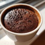 Close-up view of the airy, bubbly texture of homemade chocolate mousse in a small white cup.