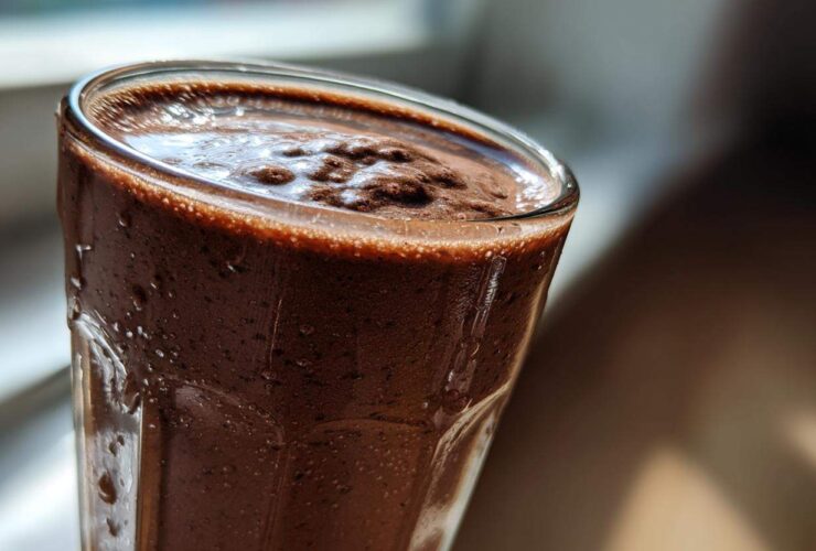 Close-up, sunlit view of a thick, blended frozen hot chocolate in a tall glass, showing condensation.