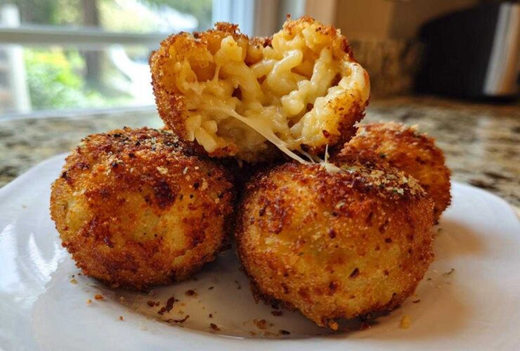 Four golden brown, deep-fried rice balls, one cut open showing melted cheese and macaroni filling.