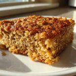 A square slice of golden brown baked oatmeal with a textured, caramelized top, sitting on a white plate.