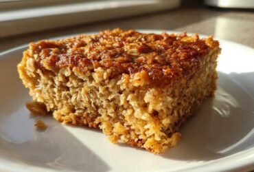 A square slice of golden brown baked oatmeal with a textured, caramelized top, sitting on a white plate.