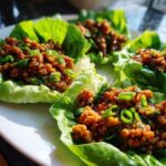 Close-up of three servings of savory chicken lettuce wraps topped with green onions.