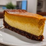 A thick slice of two-toned pumpkin cheesecake with a dark chocolate crust served on a white plate.