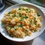 A white bowl filled with fluffy rice pilaf featuring toasted vermicelli and topped with fresh chopped parsley.