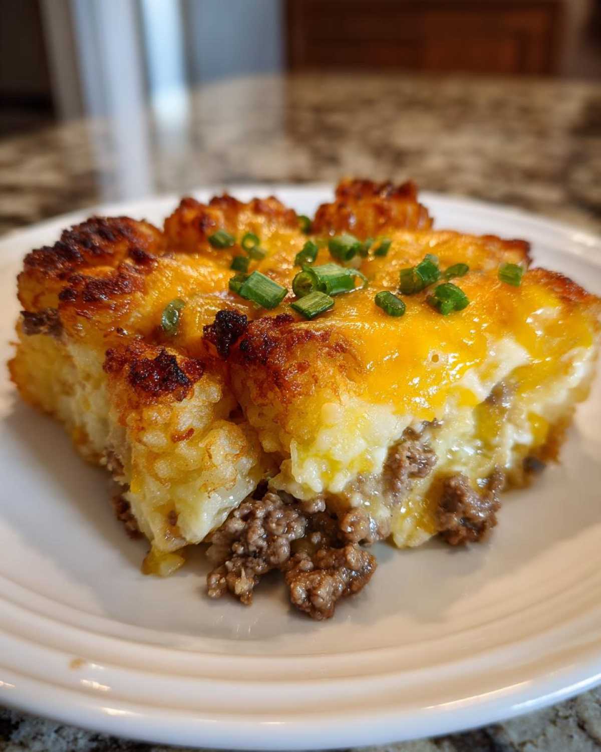 A close-up serving of tater tot casserole with browned tater tots, melted cheddar cheese, and chives.