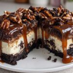 A cross-section view of a rich turtle cheesecake topped with thick chocolate ganache, dripping caramel sauce, and whole pecans.