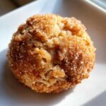 A single, freshly baked apple pie cookies coated in sparkling cinnamon sugar, resting on a white plate.