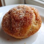 A single, round apple pie cookies heavily coated in sparkling cinnamon sugar, resting on a white plate.
