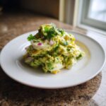 A mound of creamy avocado egg salad mixed with chunks of hard-boiled egg and red onion, garnished with fresh cilantro.