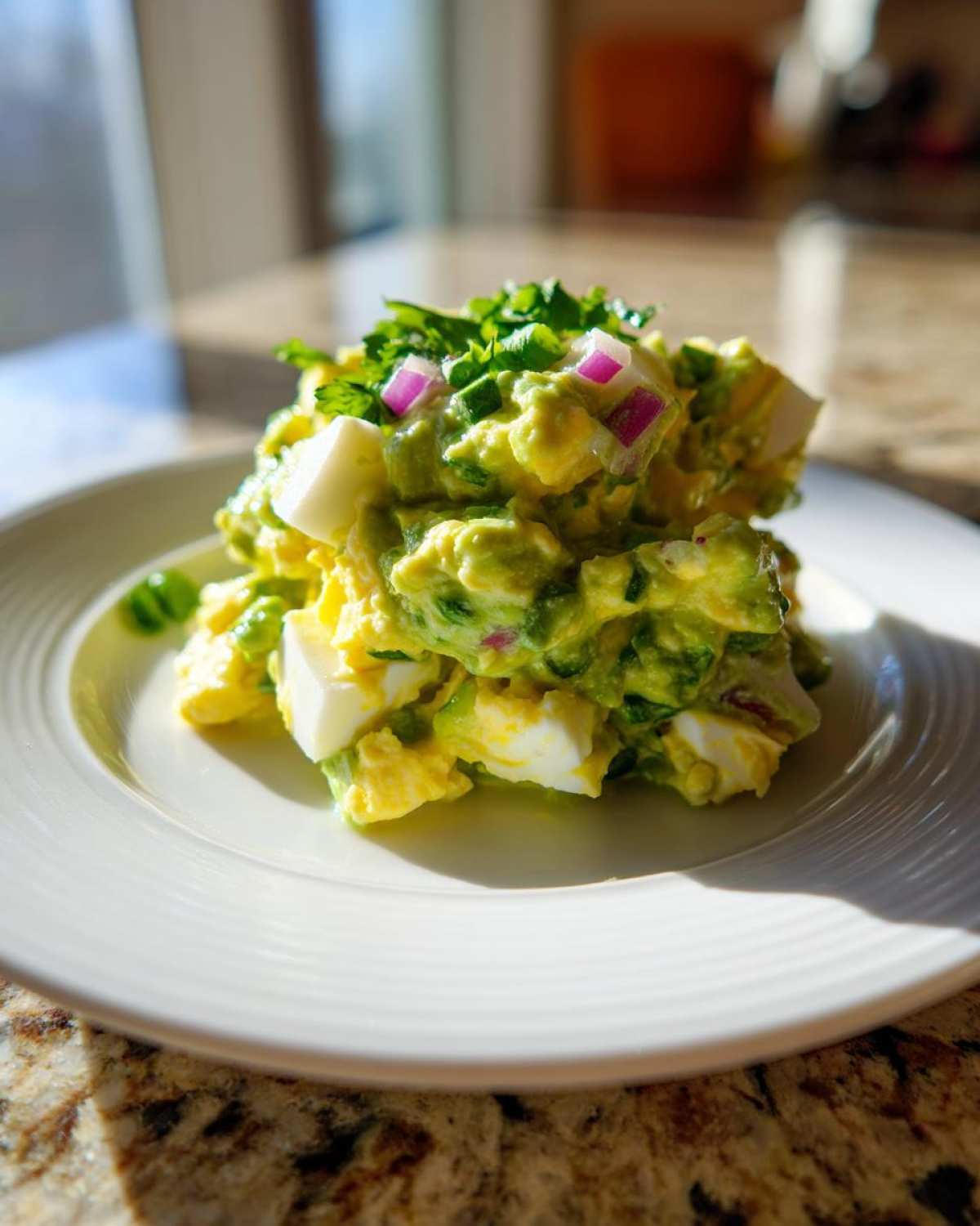 A mound of creamy avocado egg salad mixed with chunks of hard-boiled egg, topped with red onion and cilantro.