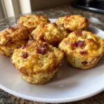 Six golden brown bacon and cheese egg bites served on a white plate, ready to eat.