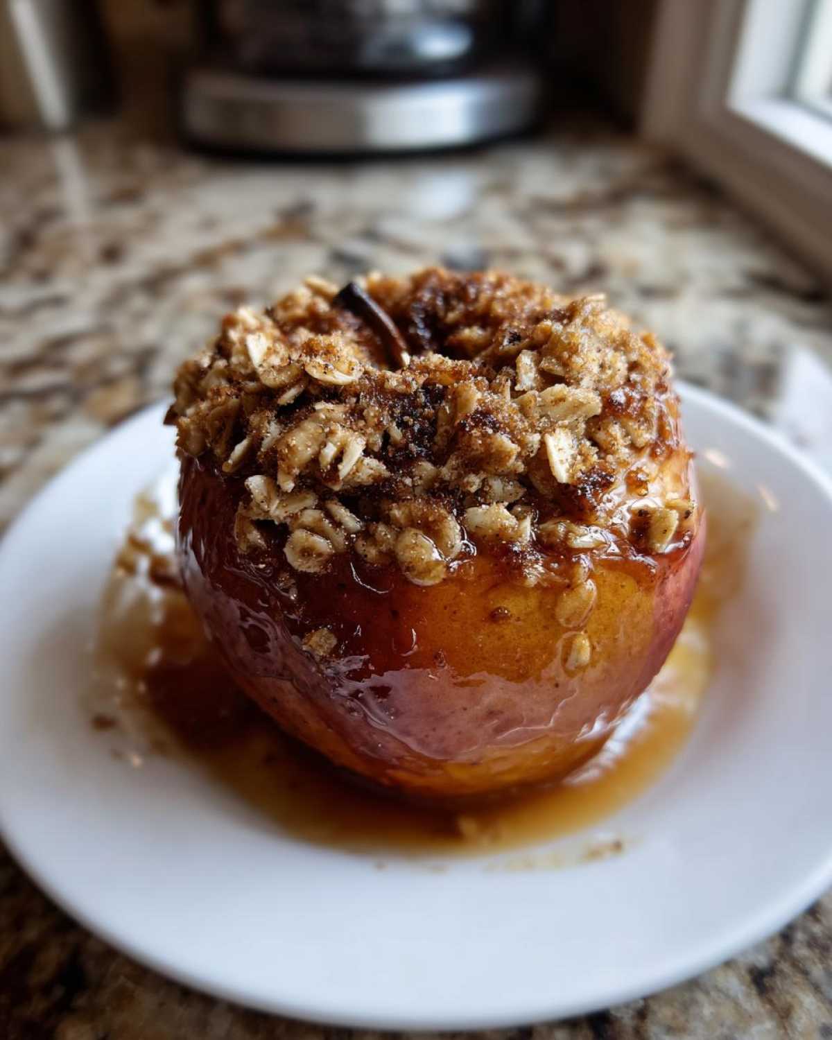 A single serving of baked apples topped with a brown sugar and oat crumble, sitting in syrup on a white plate.