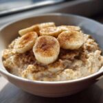 A close-up shot of creamy banana oatmeal topped with sliced bananas and sprinkled with cinnamon.