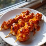 Close-up of three skewers loaded with juicy, glazed bang bang chicken skewers on a white plate.