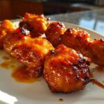 Close-up of glistening, caramelized bang bang chicken skewers served on a white plate.