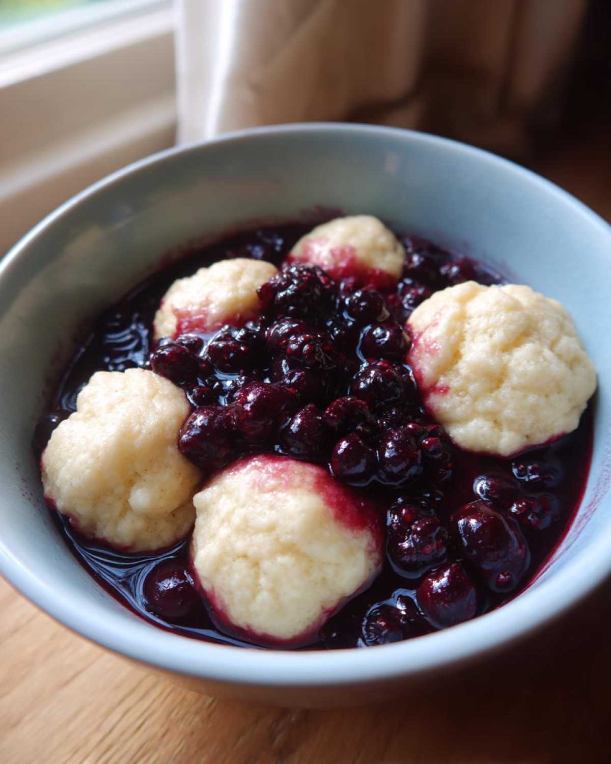 A light blue bowl filled with warm Blackberry Dumplings swimming in a rich, dark purple berry sauce.