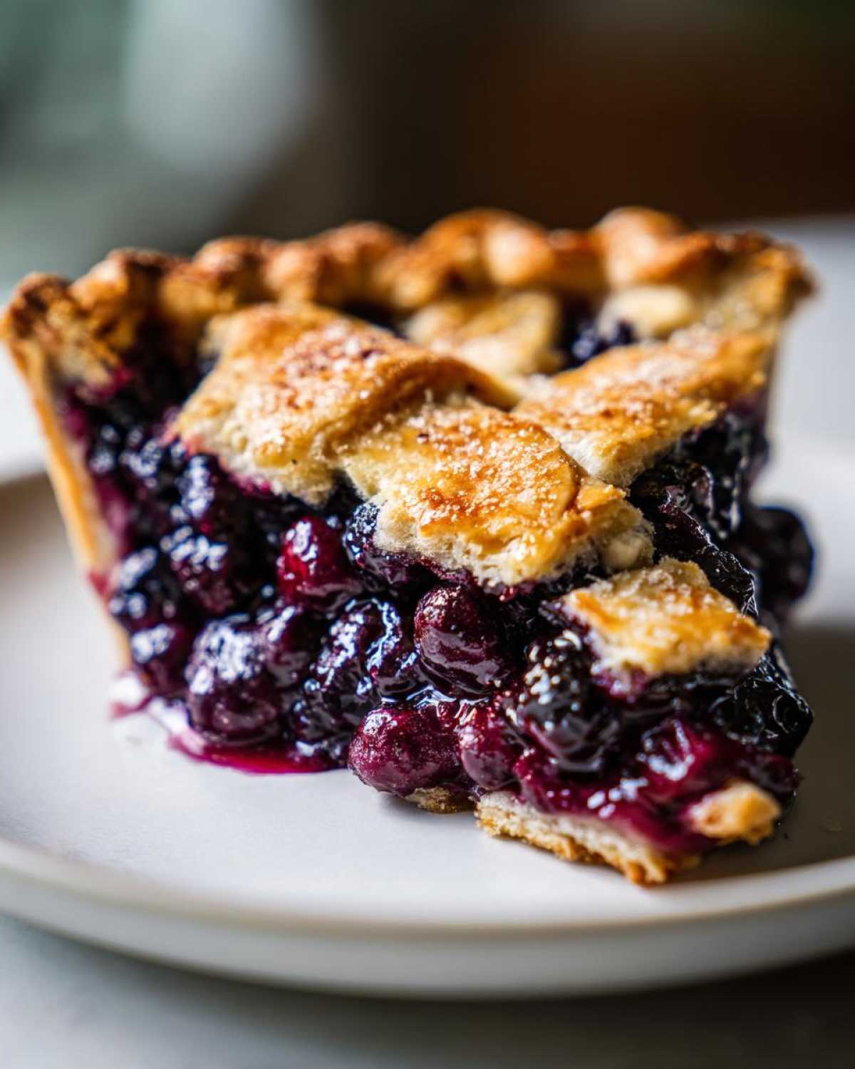 Close-up of a thick slice of blueberry pie recipe showing juicy filling and golden lattice crust sprinkled with sugar.
