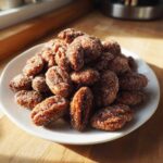 A white plate piled high with freshly made candied pecans recipe nuts coated in sparkling sugar.