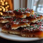 Stack of Caramel Ritz Cracker Christmas Cookies topped with chocolate and festive sprinkles, set against a blurred holiday background.