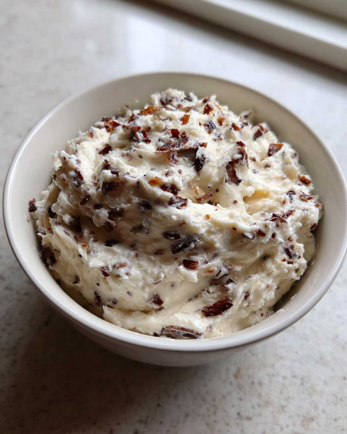 Close-up of creamy caramelized onion dip mixed with dark caramelized onions in a white bowl.