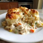 A close-up serving of creamy chicken pot pie casserole topped with golden biscuits.