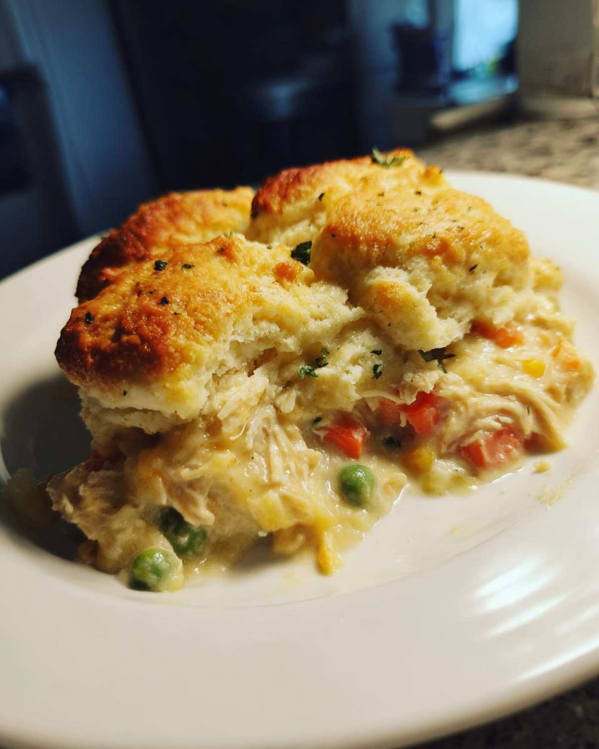A close-up serving of creamy chicken pot pie casserole topped with golden biscuits and mixed vegetables.