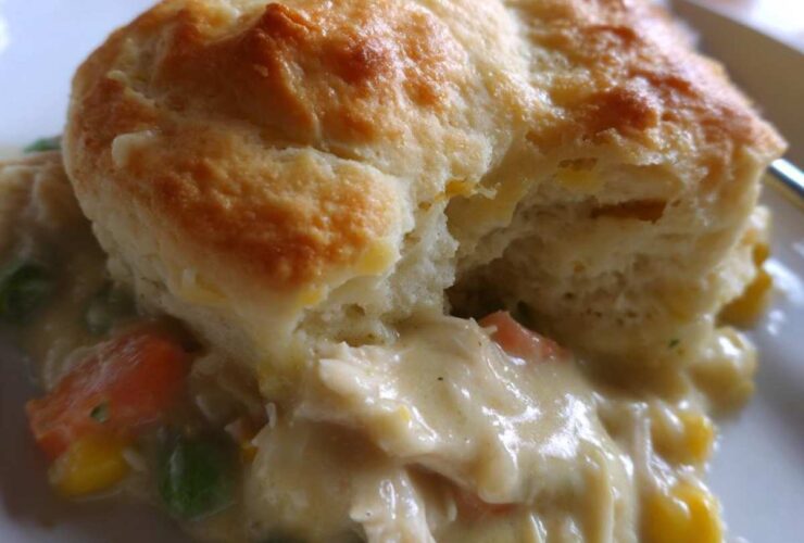 A close-up of a serving of creamy chicken pot pie casserole topped with a golden, fluffy biscuit.