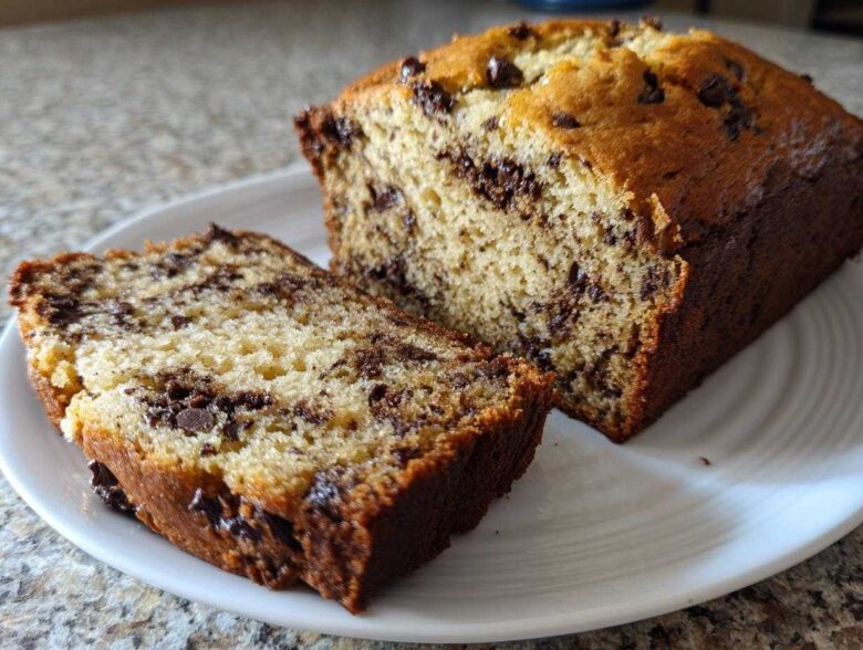 A close-up of a freshly baked chocolate chip banana bread recipe loaf, partially sliced on a white plate.