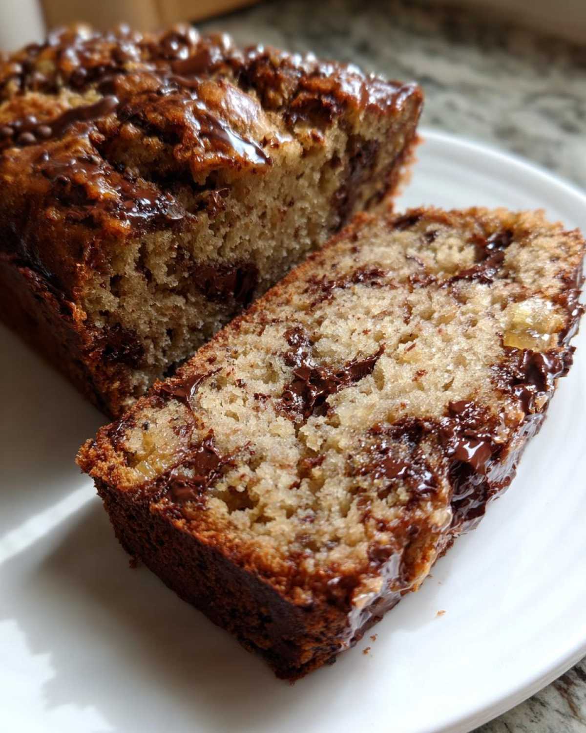 A close-up view of a thick slice of moist chocolate chip banana bread recipe, showing melted chocolate chips throughout the loaf.