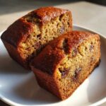 Two halves of moist mini banana bread loaves, showing chocolate chips and a rich brown crumb.