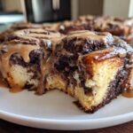A close-up of a decadent chocolate cinnamon roll slice, featuring marbled dough and a thick caramel glaze dripping down the side.