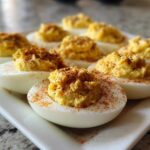 Close-up of several classic deviled eggs arranged on a white platter, topped with creamy filling and sprinkled with paprika.