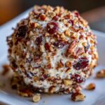 A close-up, appetizing view of a cranberry pecan cheese ball coated in chopped nuts and dried cranberries.