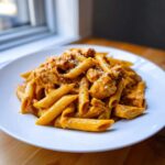 A close-up of creamy cajun chicken pasta featuring penne noodles and seasoned chicken chunks, sprinkled with cheese.