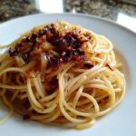 Close-up of creamy caramelized onion pasta topped with dark, crispy caramelized onions and chili flakes.