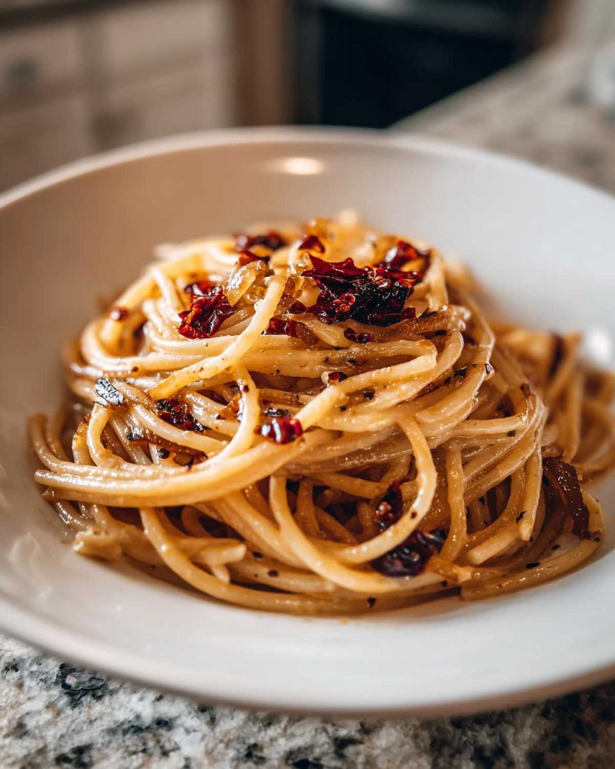 Close-up of creamy caramelized onion pasta tossed with chili flakes, served in a white bowl.