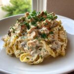 A generous serving of creamy chicken alfredo pasta topped with diced chicken and fresh chopped parsley.