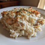 A close-up serving of creamy chicken and rice casserole topped with melted, browned cheese and parsley.