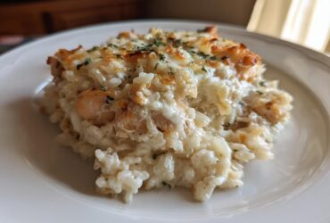 A close-up serving of creamy chicken and rice casserole topped with melted, browned cheese and parsley.