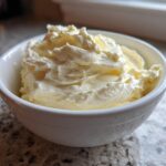 A small white bowl filled with freshly whipped, creamy garlic aioli sitting on a granite countertop.