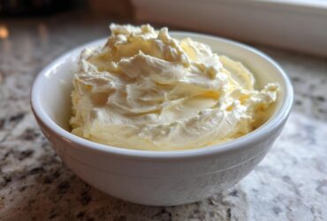 A small white bowl filled with freshly whipped, creamy garlic aioli sitting on a granite countertop.