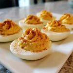 Close-up of creamy, piped deviled eggs sprinkled with paprika on a white serving platter.