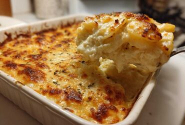 A scoop of creamy scalloped potatoes being lifted from a baking dish showing a golden-brown cheesy crust.