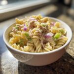 A close-up of creamy Tuna pasta salad made with rotini pasta, tuna, celery, and red onion in a white bowl.