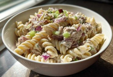 A close-up of creamy Tuna pasta salad made with rotini pasta, tuna, red onion, and celery in a white bowl.