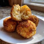 Close-up of crispy fried rice balls, one split open showing melted cheese stretching inside the rice mixture.