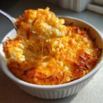 A spoonful of creamy crockpot cheesy potatoes showing a dramatic cheese pull from the baked casserole.