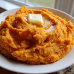 A close-up of creamy, bright orange mashed sweet potatoes topped with a melting pat of butter.