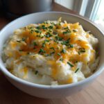 A white bowl filled with creamy easy crockpot potato soup topped with melted cheddar cheese and fresh chopped chives.